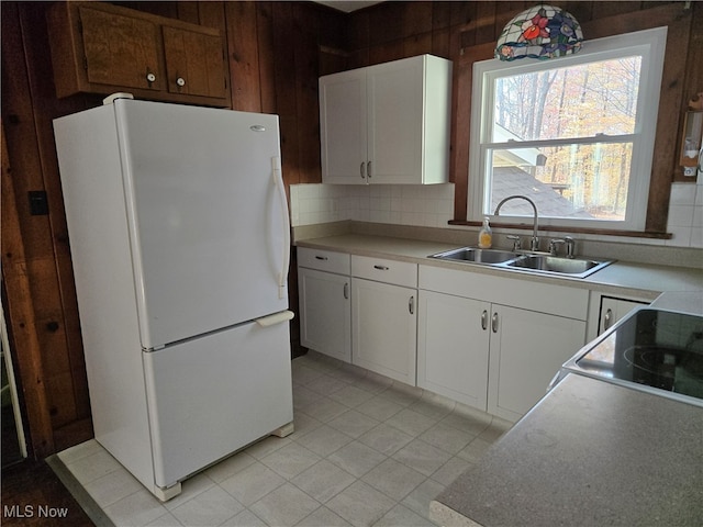 kitchen with white refrigerator, decorative backsplash, wood walls, sink, and white cabinetry