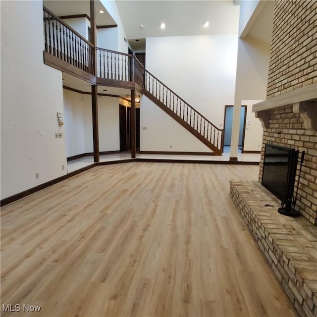 unfurnished living room featuring a towering ceiling, a fireplace, and light hardwood / wood-style floors