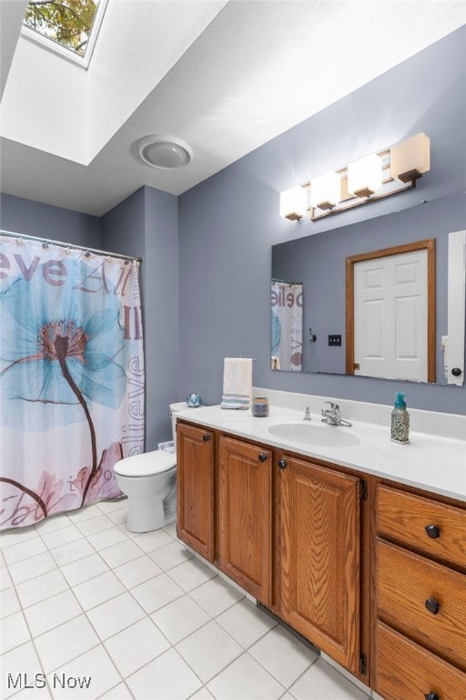 bathroom featuring tile patterned flooring, vanity, toilet, and a skylight