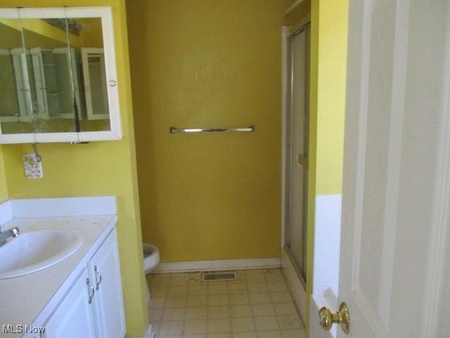 bathroom with tile patterned flooring, vanity, toilet, and a shower with door