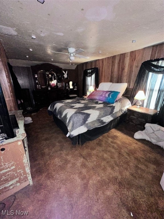 bedroom featuring ceiling fan, wooden walls, and dark carpet