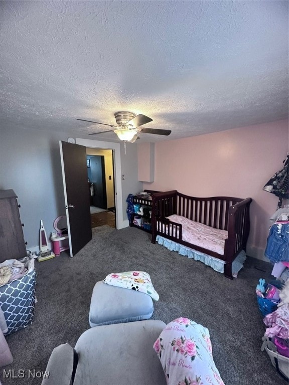 carpeted bedroom featuring ceiling fan, a textured ceiling, and a nursery area