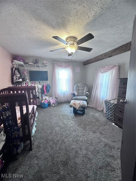 carpeted bedroom with a crib, ceiling fan, and a textured ceiling