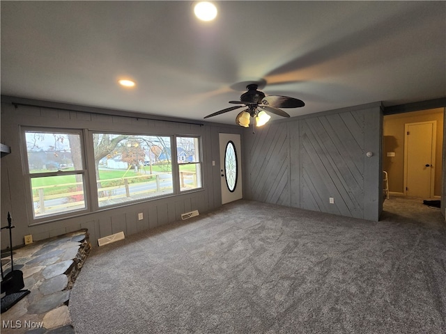 unfurnished living room featuring carpet flooring, plenty of natural light, wooden walls, and ceiling fan