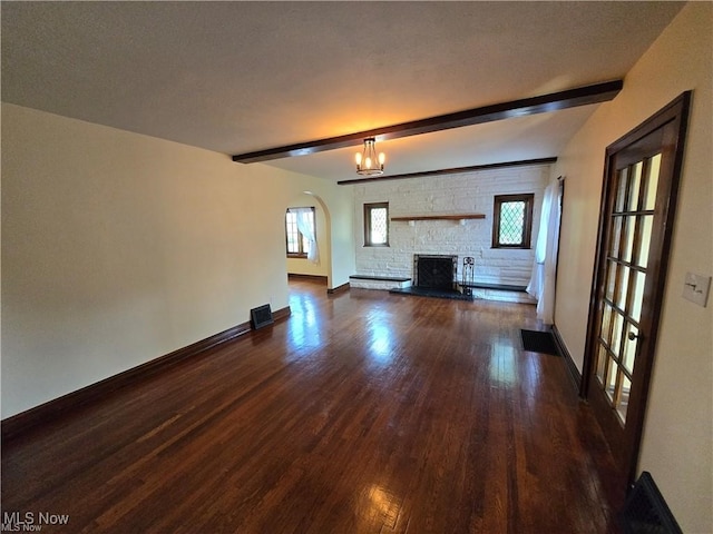 unfurnished living room featuring dark wood-type flooring, beamed ceiling, brick wall, and a fireplace