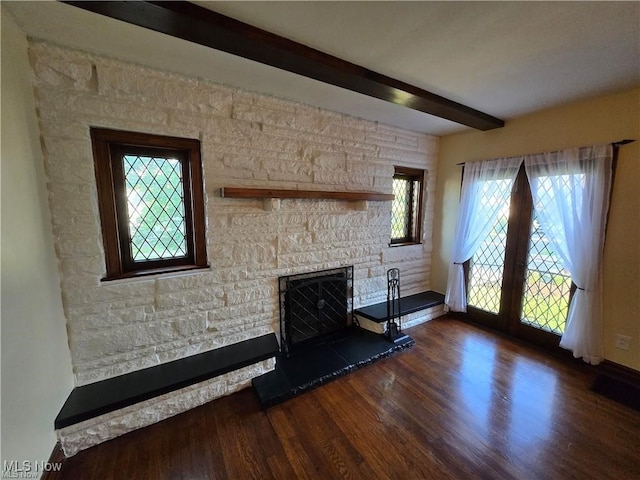 unfurnished living room with a stone fireplace, dark wood-type flooring, and beam ceiling