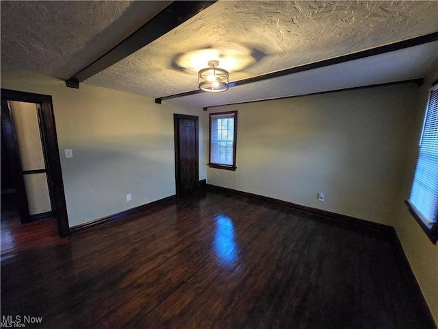 spare room with dark wood-type flooring, a textured ceiling, and beam ceiling