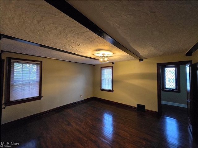 spare room with a textured ceiling, dark wood-type flooring, a healthy amount of sunlight, and beam ceiling