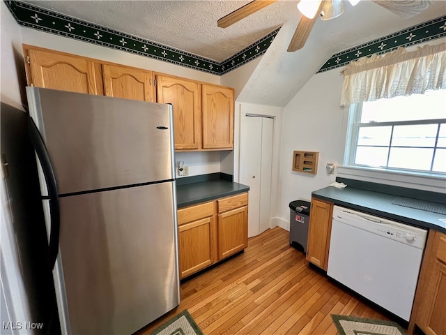 kitchen featuring vaulted ceiling, dishwasher, a textured ceiling, light wood-type flooring, and stainless steel fridge