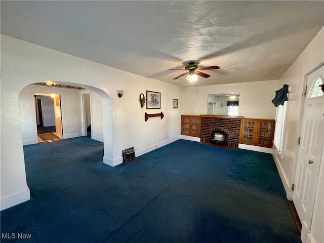 unfurnished living room featuring ceiling fan, dark carpet, and a brick fireplace