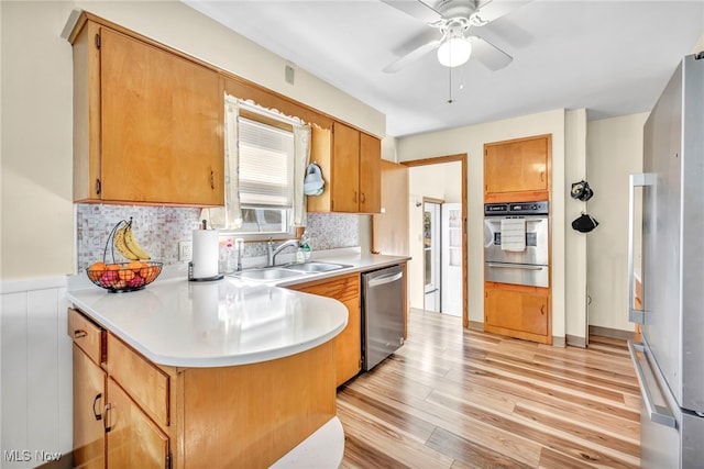 kitchen with stainless steel appliances, sink, tasteful backsplash, ceiling fan, and light wood-type flooring