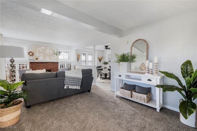 carpeted living room featuring ceiling fan, a fireplace, beamed ceiling, and a textured ceiling