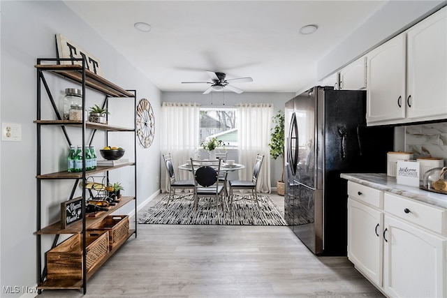 kitchen featuring white cabinets, light wood-type flooring, black fridge, and ceiling fan