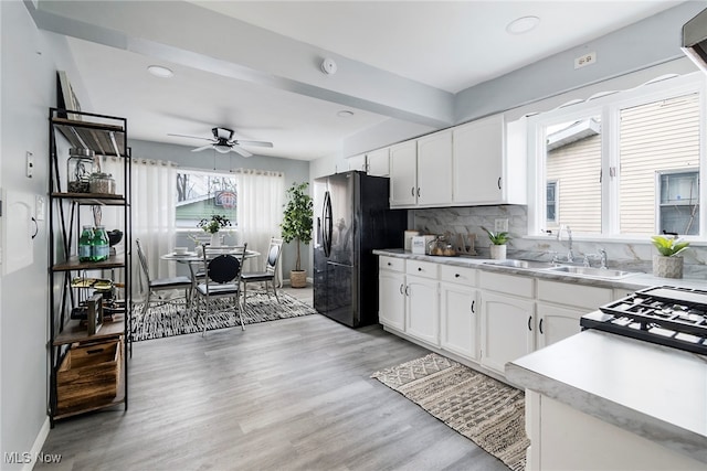 kitchen with white cabinets, black fridge, sink, ceiling fan, and light wood-type flooring