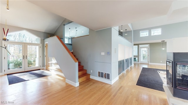 foyer entrance with light hardwood / wood-style floors, high vaulted ceiling, and french doors