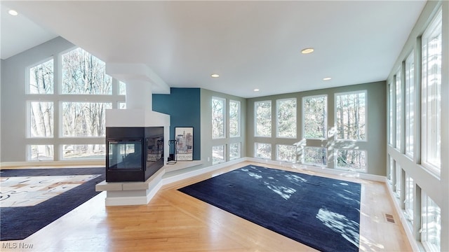 interior space with light hardwood / wood-style floors, a multi sided fireplace, and a healthy amount of sunlight