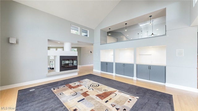 unfurnished living room with high vaulted ceiling, a multi sided fireplace, and hardwood / wood-style flooring