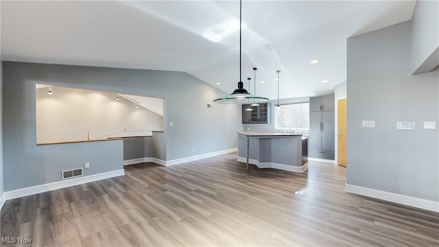 kitchen featuring a center island, vaulted ceiling, hardwood / wood-style flooring, gray cabinetry, and decorative light fixtures