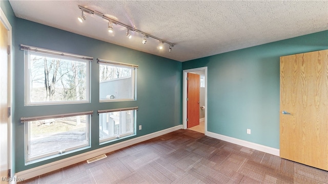 empty room with rail lighting, a textured ceiling, and parquet flooring