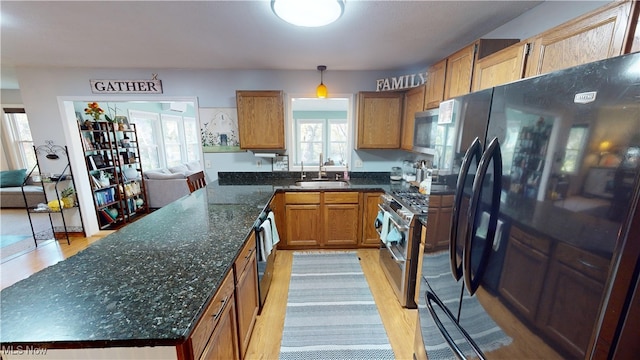 kitchen featuring pendant lighting, sink, dark stone countertops, light wood-type flooring, and appliances with stainless steel finishes