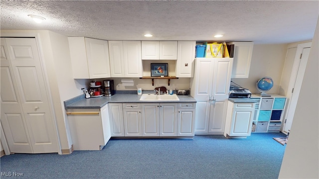 kitchen featuring sink, white cabinets, a textured ceiling, and dark colored carpet