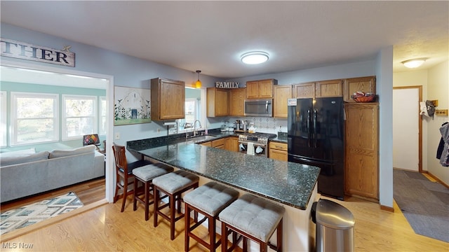 kitchen with appliances with stainless steel finishes, light wood-type flooring, hanging light fixtures, and a kitchen breakfast bar