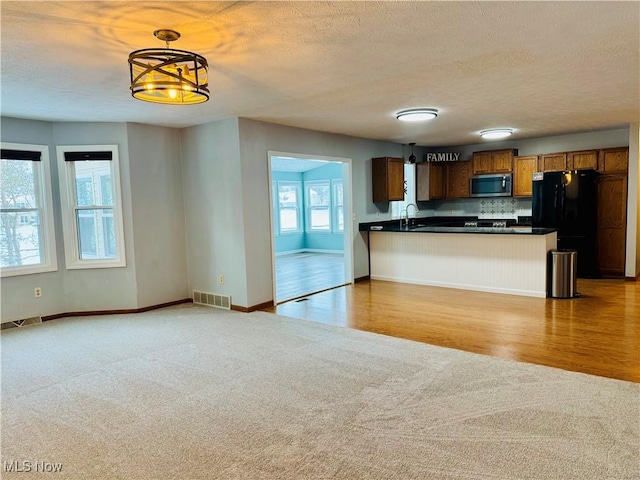 kitchen featuring kitchen peninsula, light carpet, black refrigerator, a kitchen breakfast bar, and decorative light fixtures