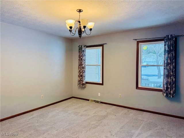 carpeted empty room with a textured ceiling, a wealth of natural light, and a chandelier