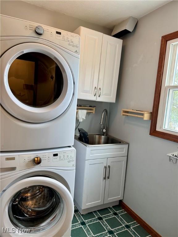 laundry area featuring cabinets, sink, and stacked washing maching and dryer