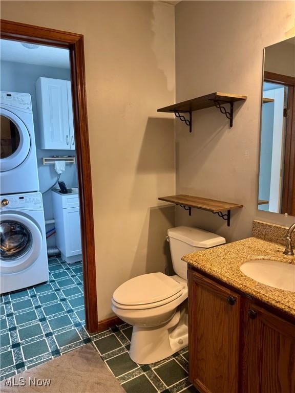 bathroom with vanity, toilet, and stacked washer and clothes dryer