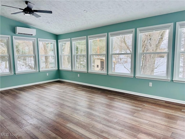 unfurnished sunroom featuring a wall mounted air conditioner, vaulted ceiling, ceiling fan, and a healthy amount of sunlight