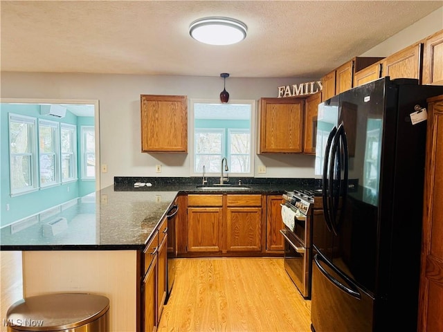 kitchen with black appliances, sink, dark stone countertops, a textured ceiling, and light hardwood / wood-style floors