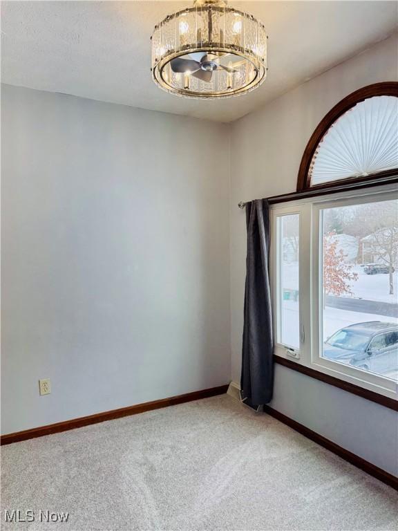 carpeted empty room featuring a notable chandelier