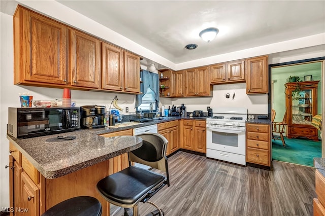 kitchen with dark hardwood / wood-style flooring, dark stone counters, white stove, a breakfast bar area, and sink