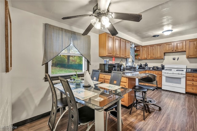 kitchen with dark wood-type flooring, sink, ceiling fan, a breakfast bar, and white range with gas stovetop