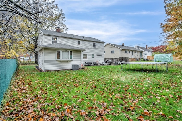 rear view of house with central AC, a trampoline, and a lawn