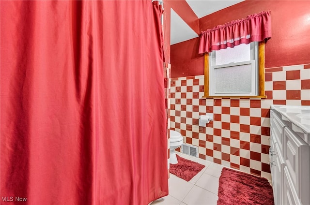 bathroom with tile walls, toilet, vanity, and tile patterned floors