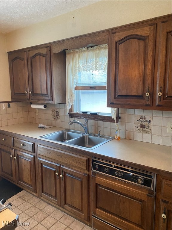 kitchen with sink, tasteful backsplash, a textured ceiling, dark brown cabinets, and paneled dishwasher