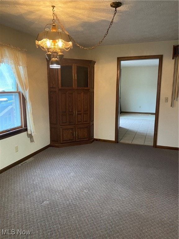 spare room featuring light carpet, a textured ceiling, and a notable chandelier