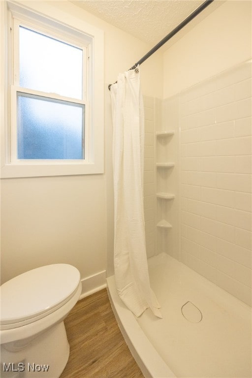 bathroom with toilet, wood-type flooring, a shower with shower curtain, and a textured ceiling