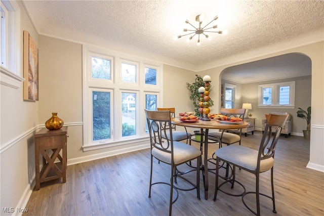 dining area featuring dark wood-type flooring, a chandelier, a textured ceiling, and crown molding