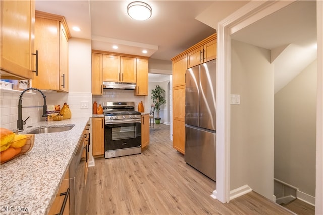 kitchen with light stone counters, light wood-type flooring, appliances with stainless steel finishes, decorative backsplash, and sink