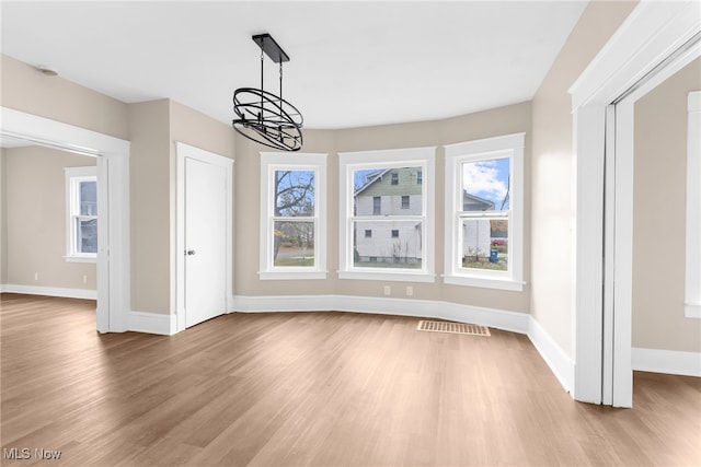 unfurnished dining area featuring a wealth of natural light, light hardwood / wood-style floors, and an inviting chandelier