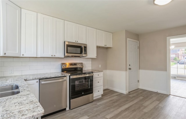 kitchen with light hardwood / wood-style flooring, light stone countertops, appliances with stainless steel finishes, and white cabinets