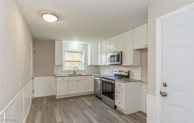 kitchen with stainless steel appliances, light hardwood / wood-style floors, sink, stone counters, and white cabinetry