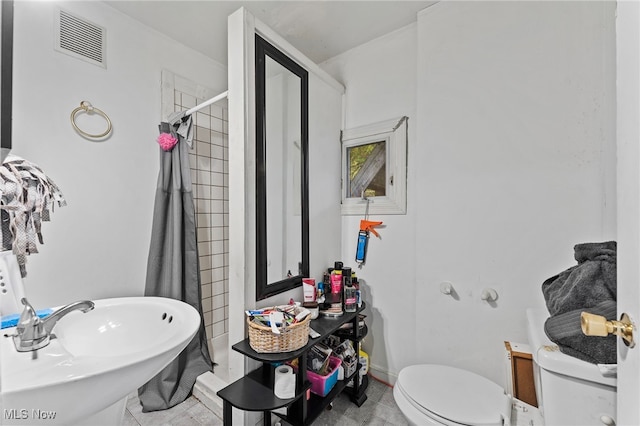 bathroom featuring toilet, sink, tile patterned flooring, and a tile shower