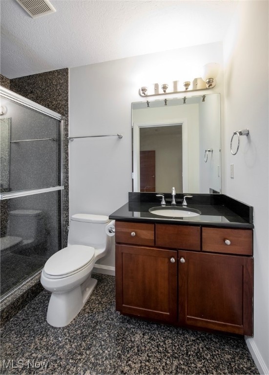 bathroom with vanity, a textured ceiling, toilet, and a shower with door