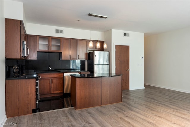 kitchen with tasteful backsplash, light wood-type flooring, appliances with stainless steel finishes, and decorative light fixtures