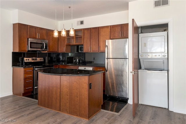 kitchen with dark wood-type flooring, a kitchen island, pendant lighting, appliances with stainless steel finishes, and stacked washer / drying machine