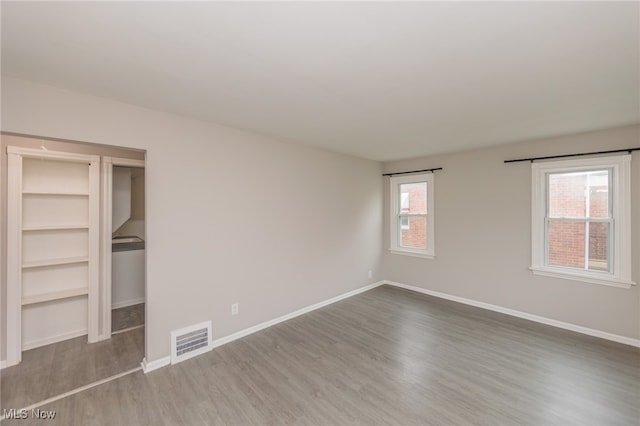 unfurnished bedroom featuring hardwood / wood-style floors, multiple windows, and a closet